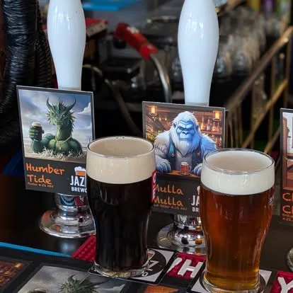 Two poured pints of Jazz BrewCo beer with pump clips behind